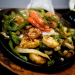 Flaco’s: Steak, Chicken and Shrimp › Served Sizzling with Green Peppers, Onions, Tomatoes, Guacamole, Sour Cream, Flour Tortillas, Rice and Refried Beans