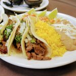 Steak Tacos >3 Marinated Strips of Beef Corn Tortilla Tacos with Fresh Onions, Cilantro, Rice and Refried Beans