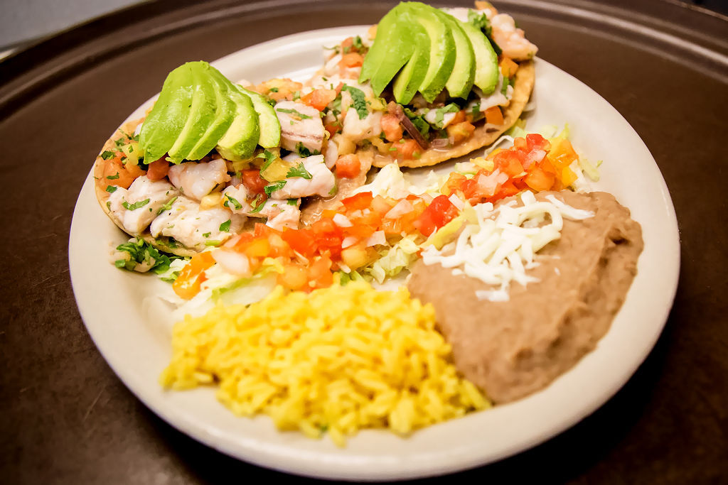 Tostadas de Ceviche (Two) are Crispy Corn Tortillas with Beans, Fresh Seafood Marinated in Lime Juice, Tomatoes, Cilantro, Rice and Refried Beans. OLE Flaco's.